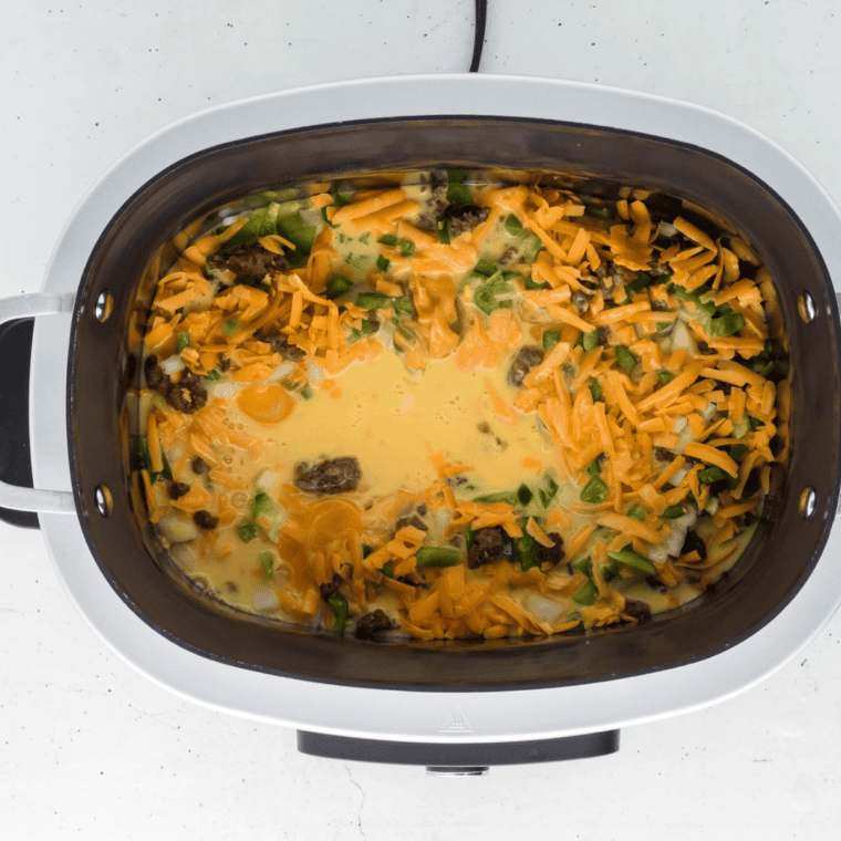Egg mixture and shredded cheese poured over the casserole layers in the slow cooker