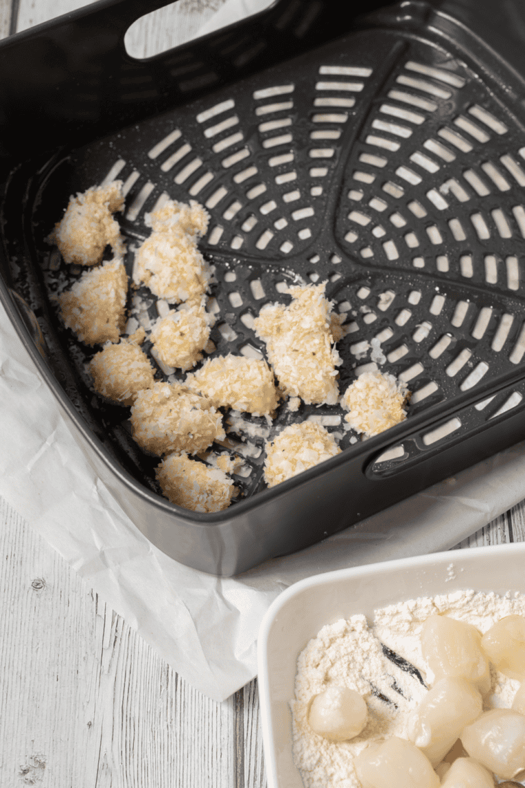Breaded scallops arranged in air fryer basket, cooking to golden and crispy perfection.