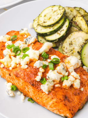 Crispy Air Fryer Buffalo Salmon fillet topped with buffalo sauce and garnished with herbs on a plate.