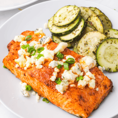 Crispy Air Fryer Buffalo Salmon fillet topped with buffalo sauce and garnished with herbs on a plate.