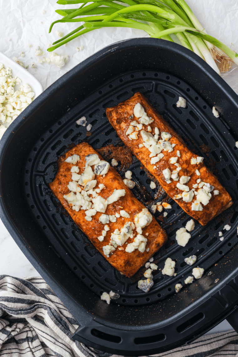 Crispy Air Fryer Buffalo Salmon fillet topped with buffalo sauce and garnished with fresh herbs on a plate.