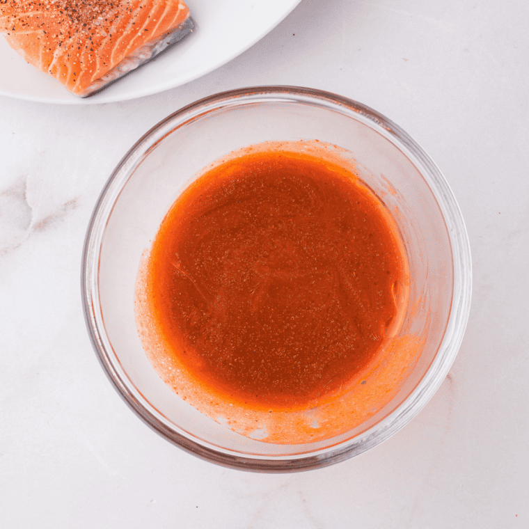 Buffalo sauce and olive oil being mixed in a small bowl, then brushed over salmon fillets.