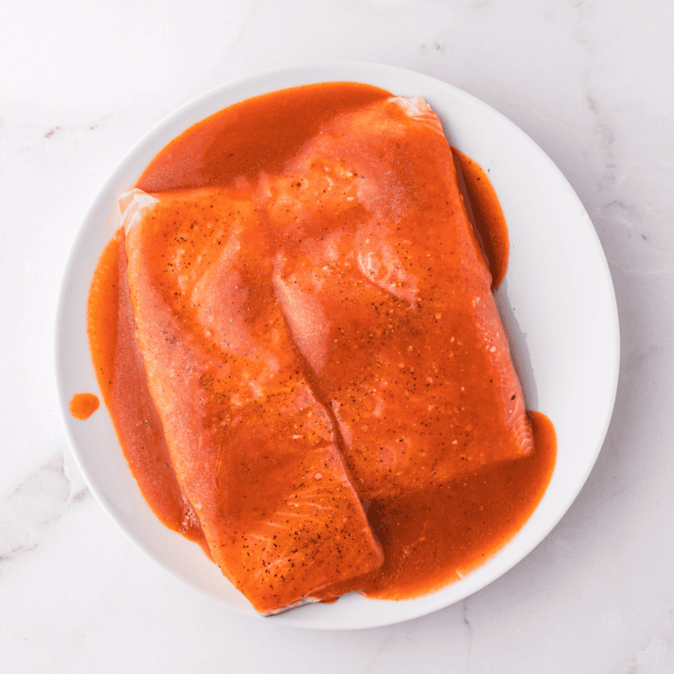 Buffalo sauce mixture being generously brushed over salmon fillets for an even coat.
