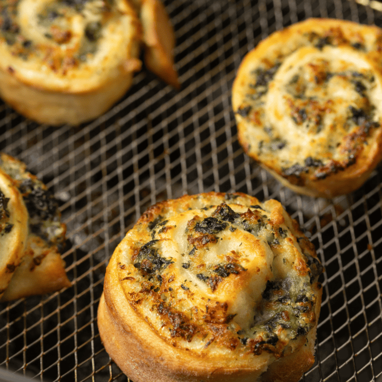 Flaky golden spinach and garlic rounds cooked in the air fryer, stacked on a plate ready to serve