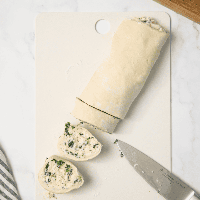 Rolling pizza dough into a tight log and slicing into 1-inch spiraled rounds filled with spinach and cheese