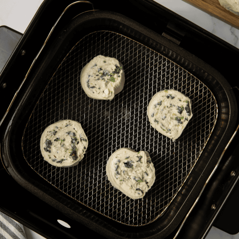 Spinach garlic rounds arranged in a single layer in an air fryer basket, ready to cook until golden and flaky