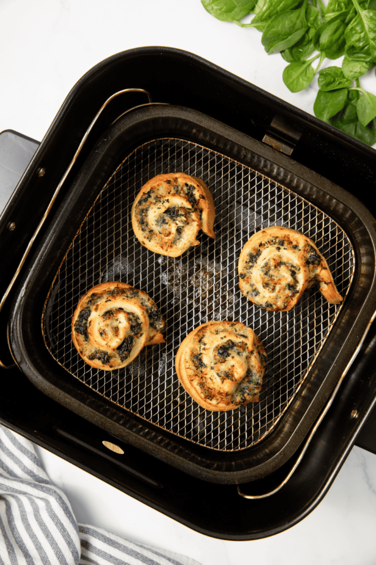Golden brown air fryer spinach garlic rounds stacked on a plate, showing flaky layers and melted cheese filling