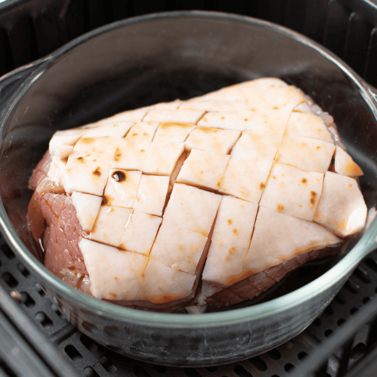 Gammon placed in air fryer basket with water underneath, cooking at 320°F until tender and fully cooked