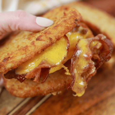 Crispy Air Fryer Hash Brown Breakfast Sandwich stacked with egg, cheese, and sausage, served on a wooden board.