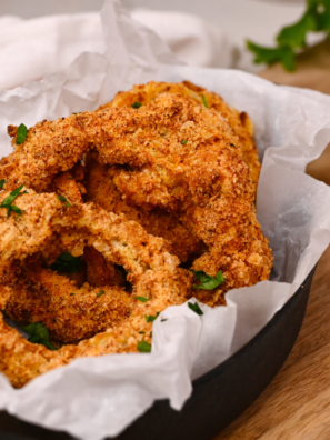 Golden, crispy keto onion rings cooked in the air fryer and served with a dipping sauce on a white plate.