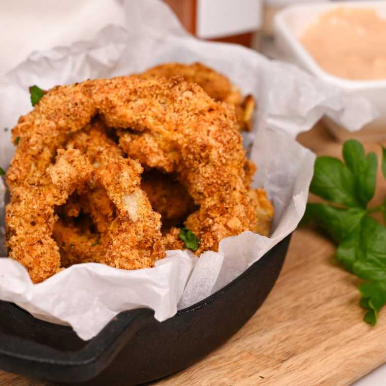 Stack of crispy, golden keto onion rings cooked in an air fryer, served with a side of dipping sauce.
