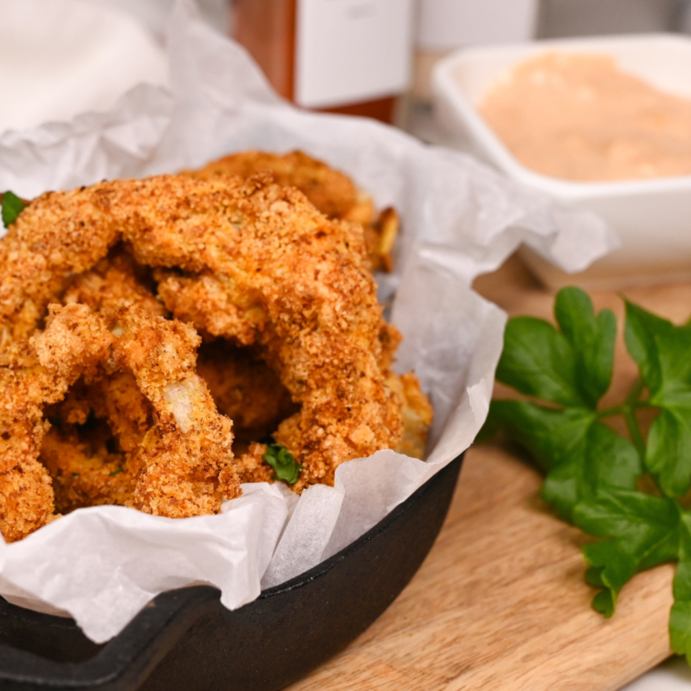 Crispy, golden keto onion rings made in the air fryer with a gluten-free almond flour and pork rind coating, served with dipping sauce.