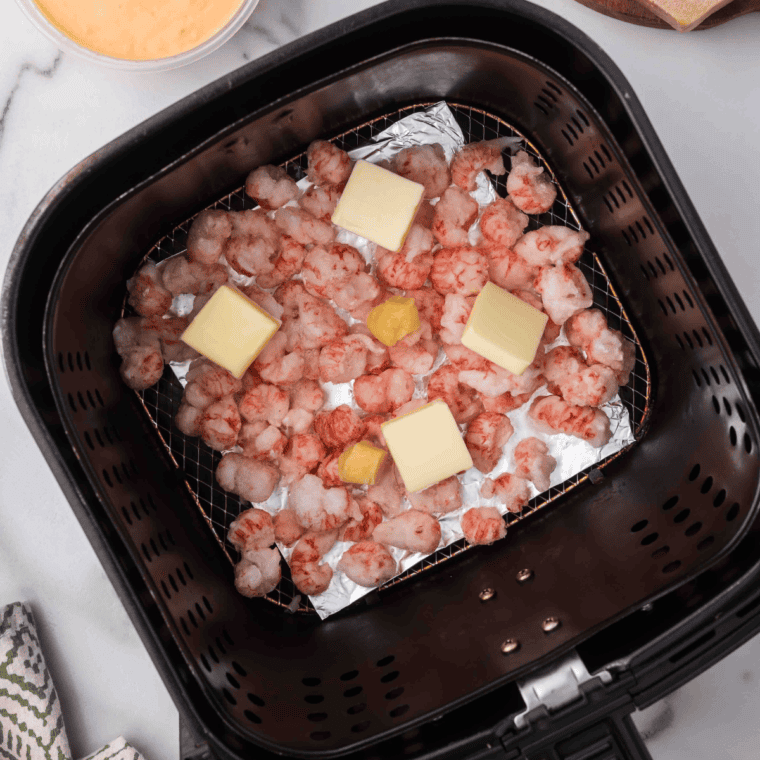 Langoustine tails with butter and garlic cooking in an air fryer basket, meat side up, lightly browned and perfectly cooked.