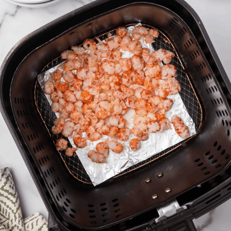 Langoustine tails arranged meat side up in an air fryer basket, sizzling with melted butter and garlic, golden and perfectly tender.