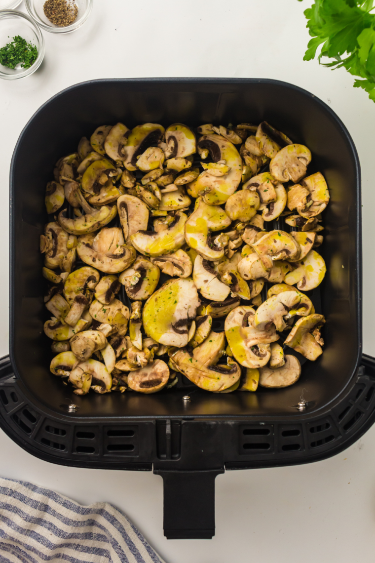 Seasoned mushrooms cooking in an air fryer basket at 375°F until golden and tender.