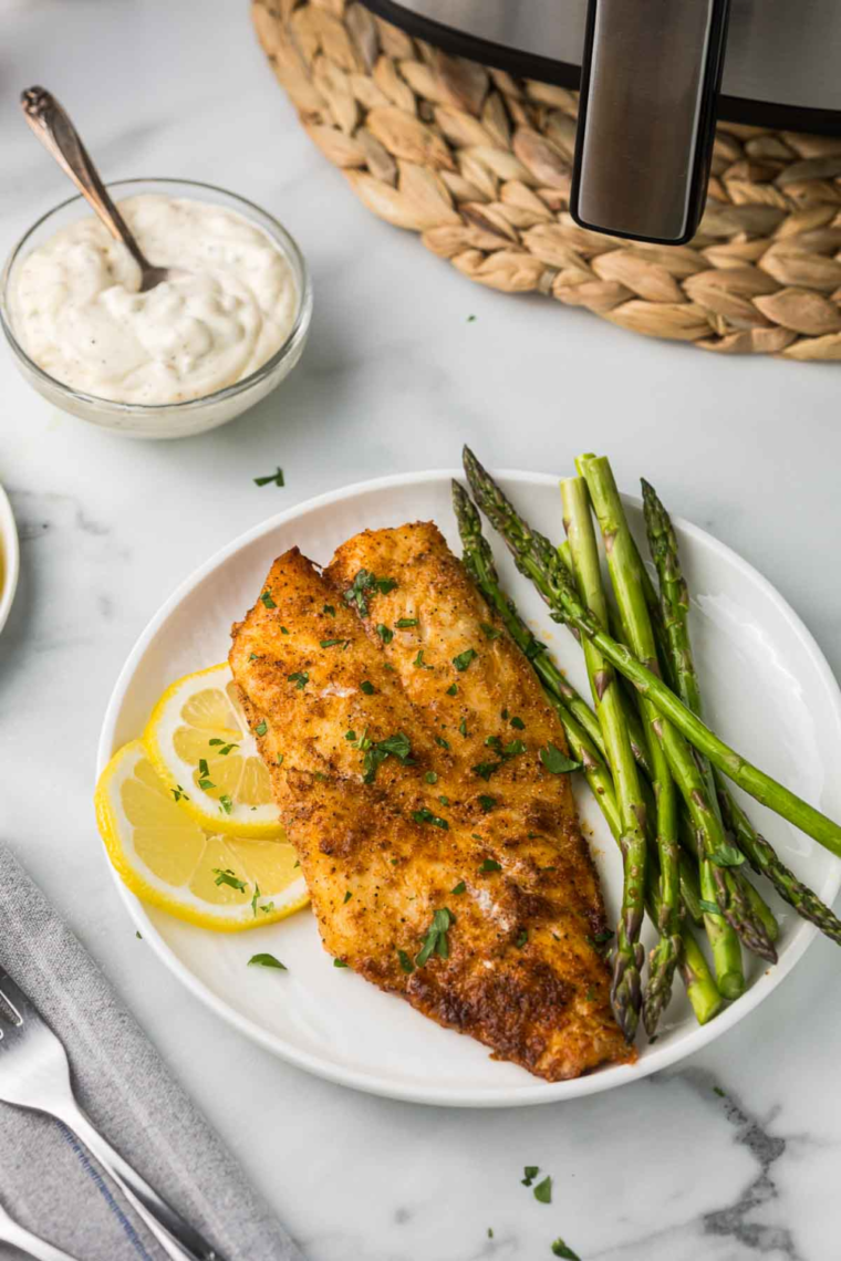 Flaky, golden-brown air fryer orange roughy fillet served with lemon wedges and parsley on a white plate.