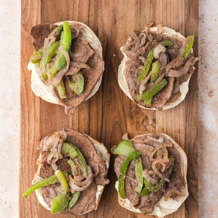 Bagel halves topped with hot steak, peppers, onions, and provolone cheese, ready for the air fryer at 375°F.