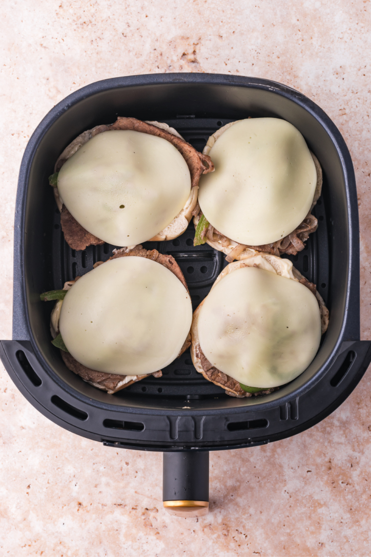Bagel halves in air fryer basket cooking at 375°F until cheese is melted and bagels are toasted.