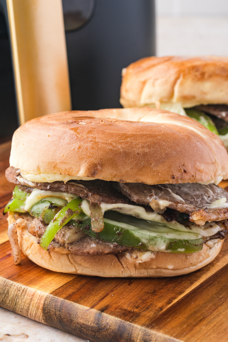 Close-up of a Philly Cheesesteak Bagel Sandwich with melted provolone, sautéed onions and peppers, and thinly sliced steak on a toasted bagel.