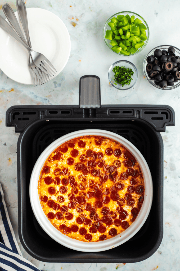 Air fryer Pepperoni Pierogy Pizza Casserole topped with melted cheese, mini pepperoni, and fresh pizza toppings in a casserole dish.