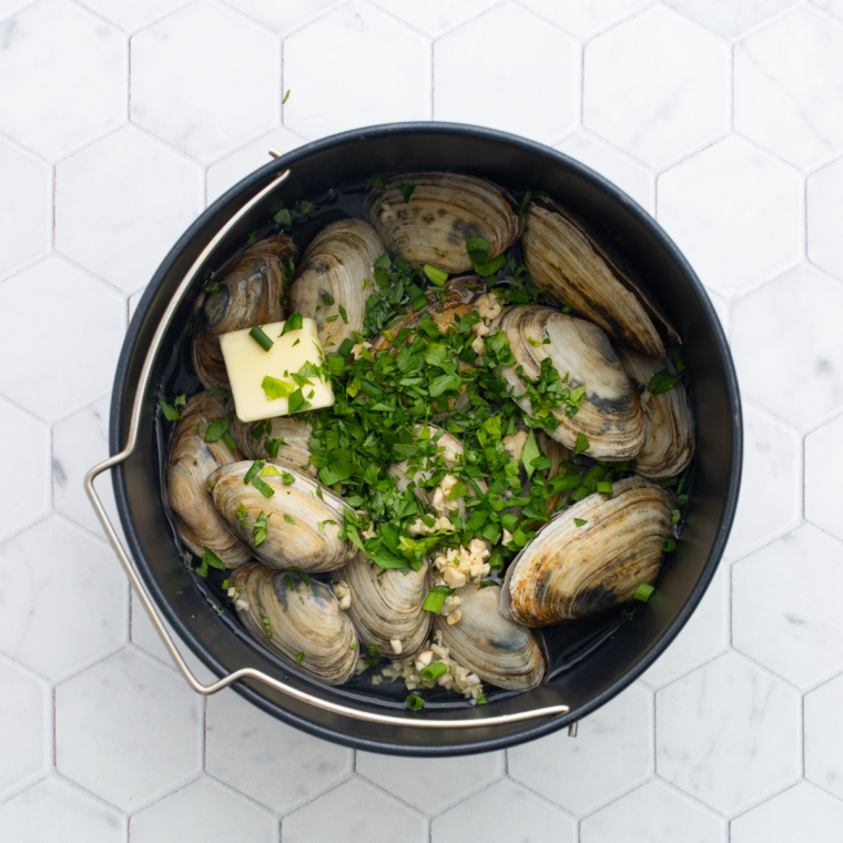 Butter, garlic, herbs, and liquid in an air fryer-safe pan, ready as a flavorful base for steamed clams.