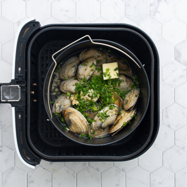 Mussels in a pan inside an air fryer basket, cooking until shells open fully.