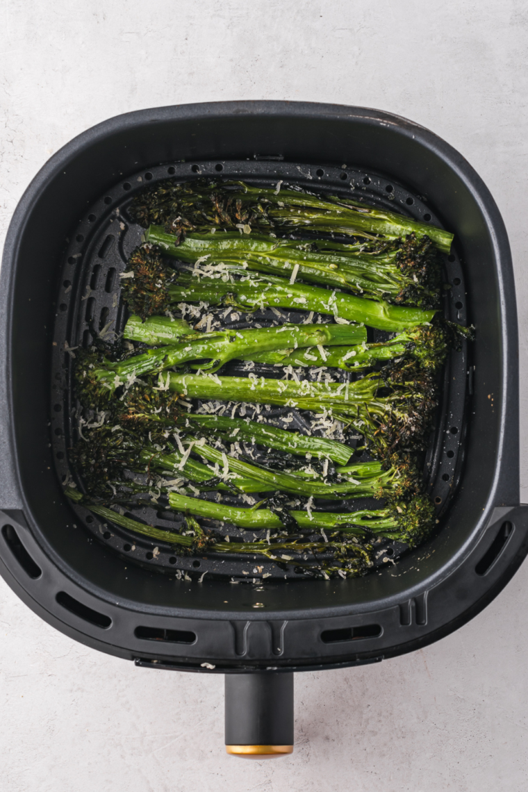 Seasoned tenderstem broccoli in a single layer in the air fryer basket, cooking to crispy perfection.