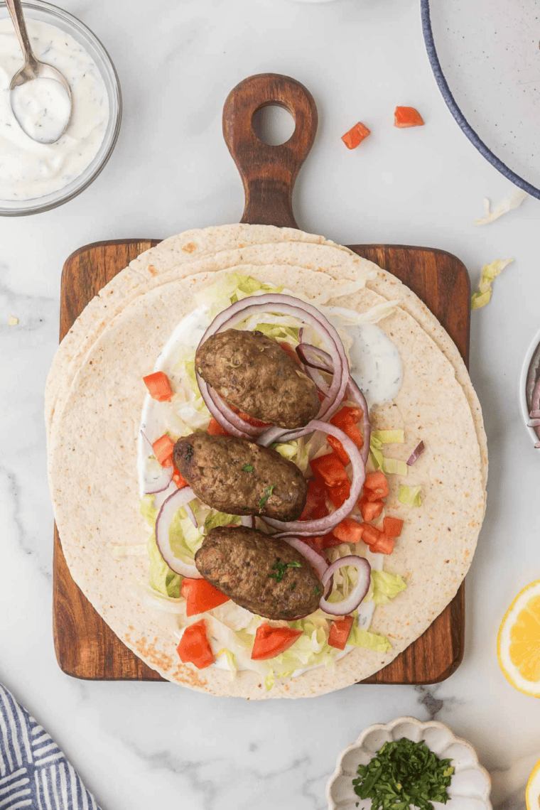 Assembling Air Fryer Turkish Lamb Wraps on wooden cutting board.