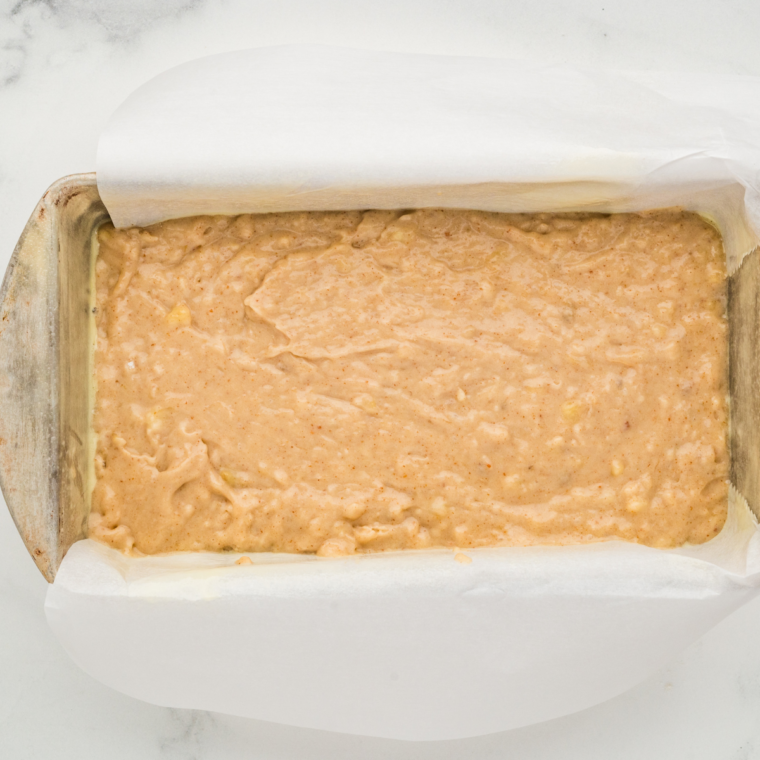 Pouring banana bread batter into a loaf pan and smoothing the top before baking.