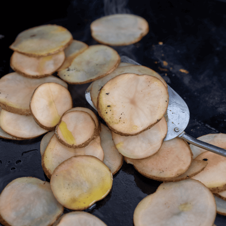 Sprinkling kosher salt and pepper over potato chips cooking on the Blackstone griddle