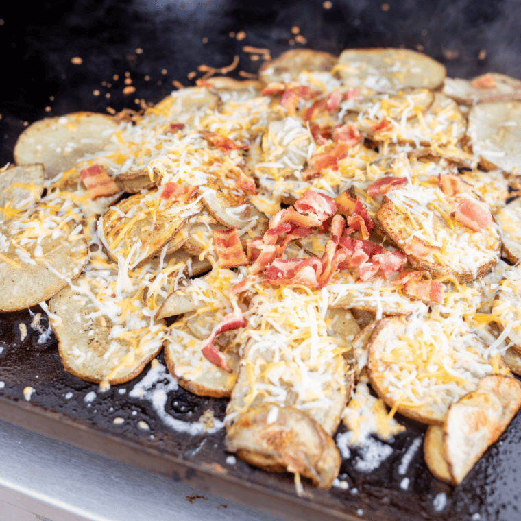 Golden Blackstone potato chips topped with shredded cheese and bacon crumbles melting on the griddle