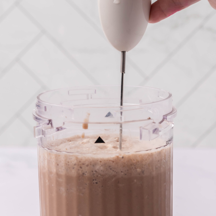 Steaming milk in a saucepan and frothing it with a handheld milk frother for a mocha latte.