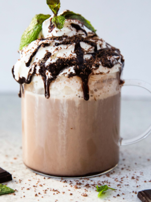 Homemade café mocha latte in a clear mug topped with foam and a sprinkle of cocoa powder.