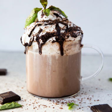 Homemade café mocha latte in a clear mug topped with foam and a sprinkle of cocoa powder.