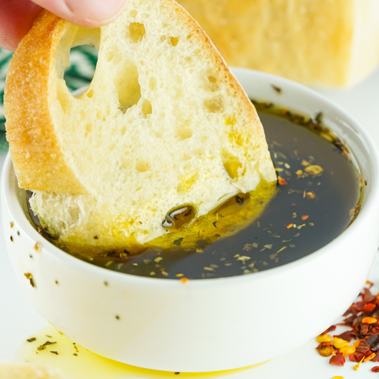 Small bowl of herbed olive oil dipping sauce served with slices of crusty bread.