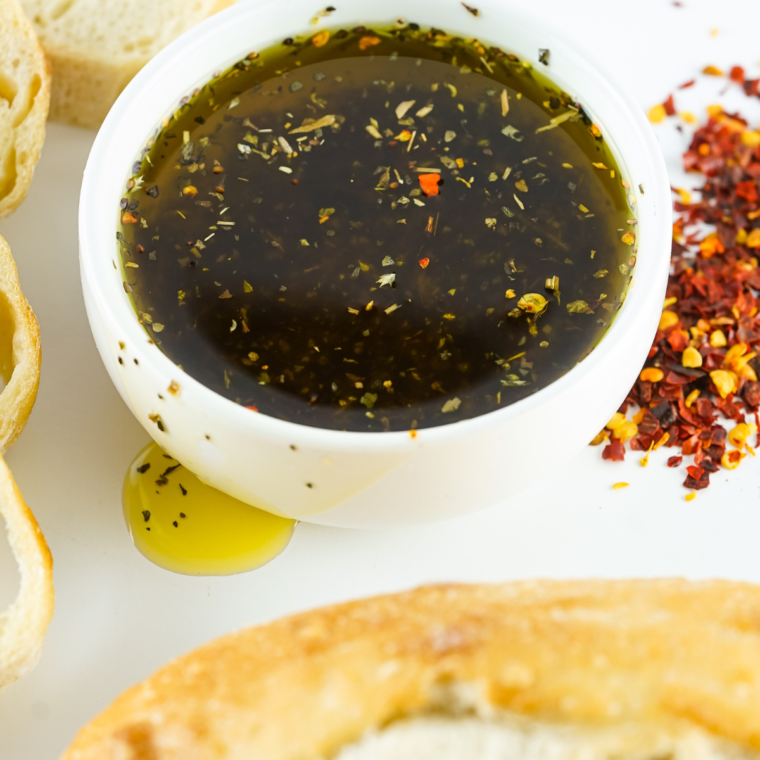 Small bowl of herb-infused olive oil served with sliced crusty bread on a wooden board.
