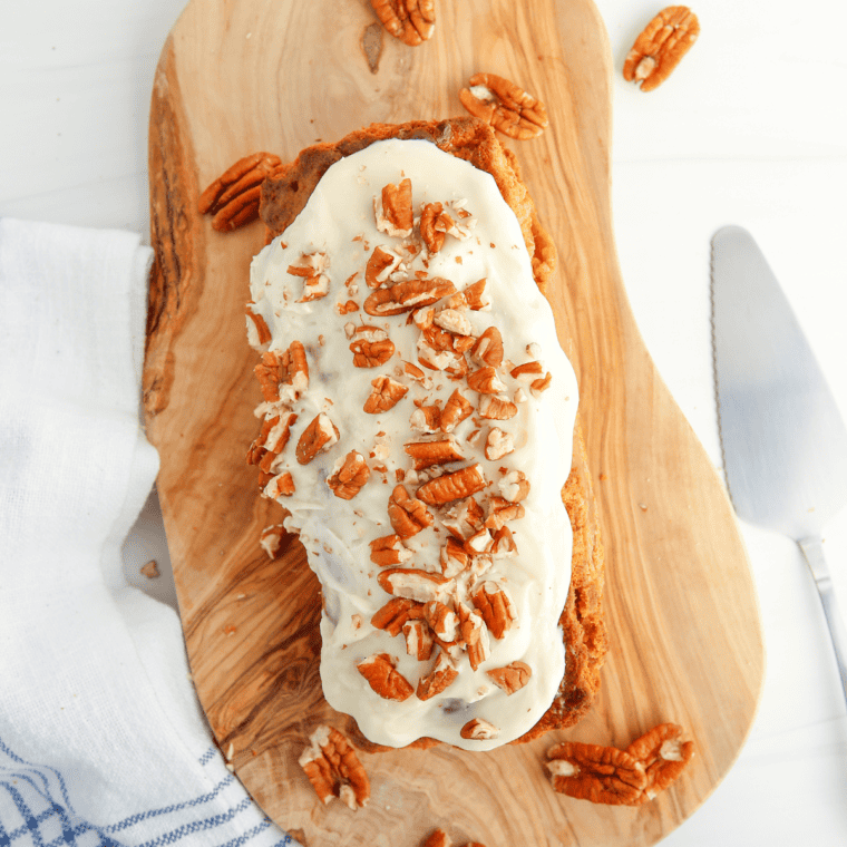 A slice of moist Cracker Barrel-inspired carrot cake topped with smooth cream cheese frosting and sprinkled with chopped pecans, served on a plate.`