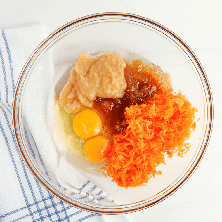 Gradually folding in eggs, oil, vanilla extract, grated carrots, and crushed pineapple into the dry mixture, followed by pecans and shredded coconut (if using), until well combined.