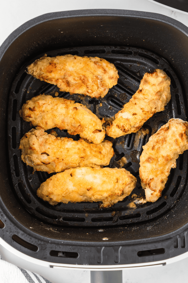 Air fryer cooking chicken tenders for 12-15 minutes, flipping halfway through until golden brown and fully cooked.