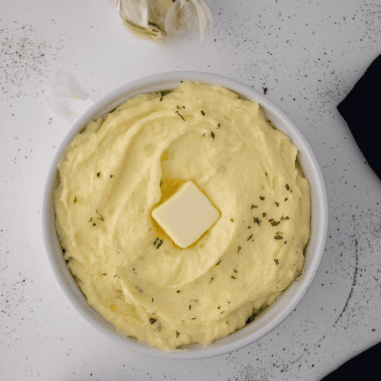 Bowl of creamy Cracker Barrel Mashed Potatoes topped with butter and fresh herbs