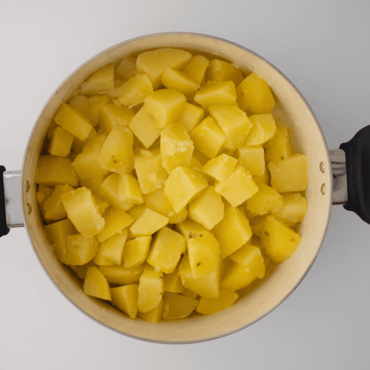 Hot cooked potatoes being mashed in a pot with a masher