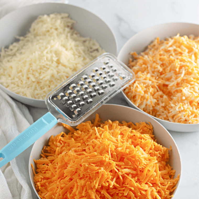 Bowl of 3 freshly grated cheese on kitchen table.
