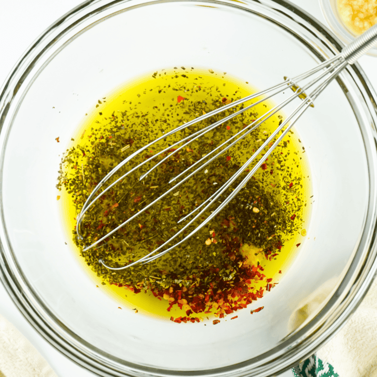 Stirring garlic and dried herbs into olive oil to make Greek dipping oil for bread