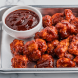 Small bowl of homemade KFC-style honey BBQ sauce with a brush and grilled chicken pieces nearby.