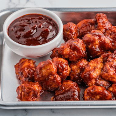 Small bowl of homemade KFC-style honey BBQ sauce with a brush and grilled chicken pieces nearby.