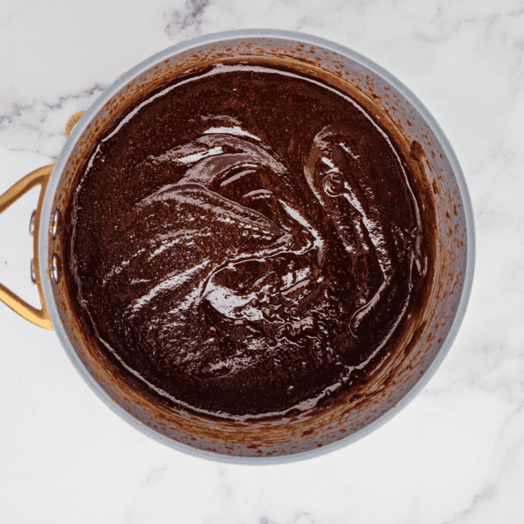 Simmering honey BBQ sauce in a saucepan, gently thickening while being stirred over low heat.