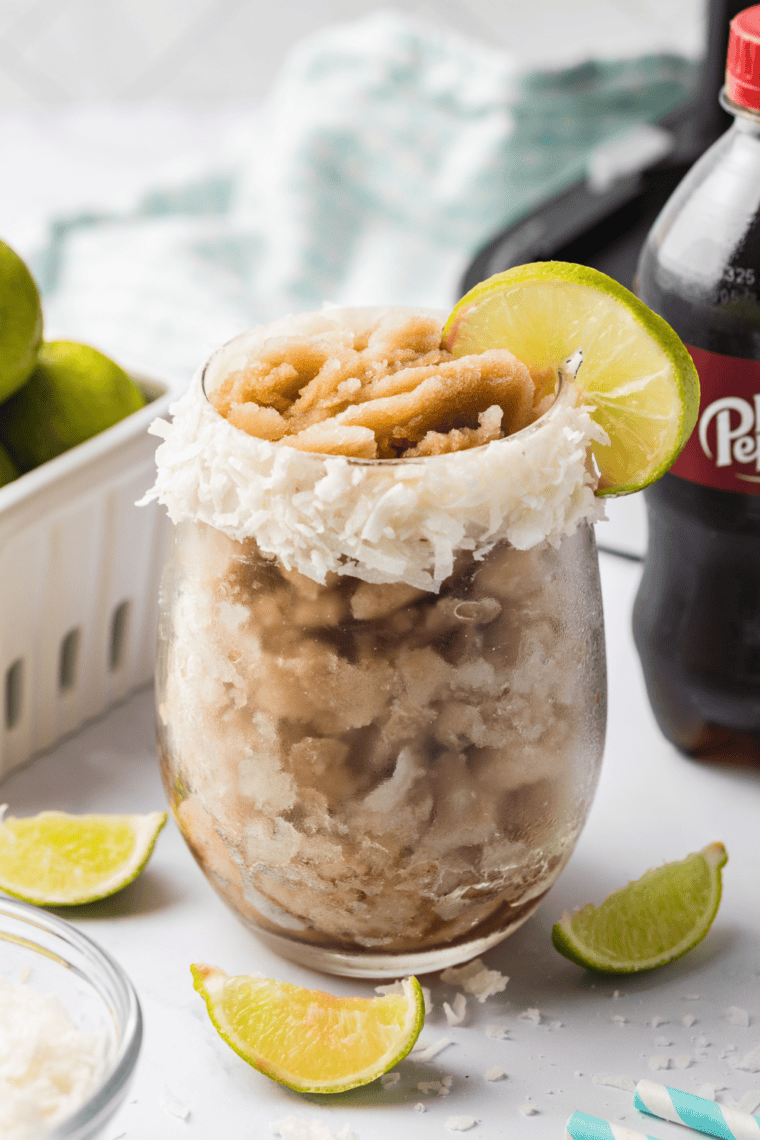 Frosty Ninja Creami Dirty Dr Pepper Slush with coconut and lime served in a clear glass with a straw