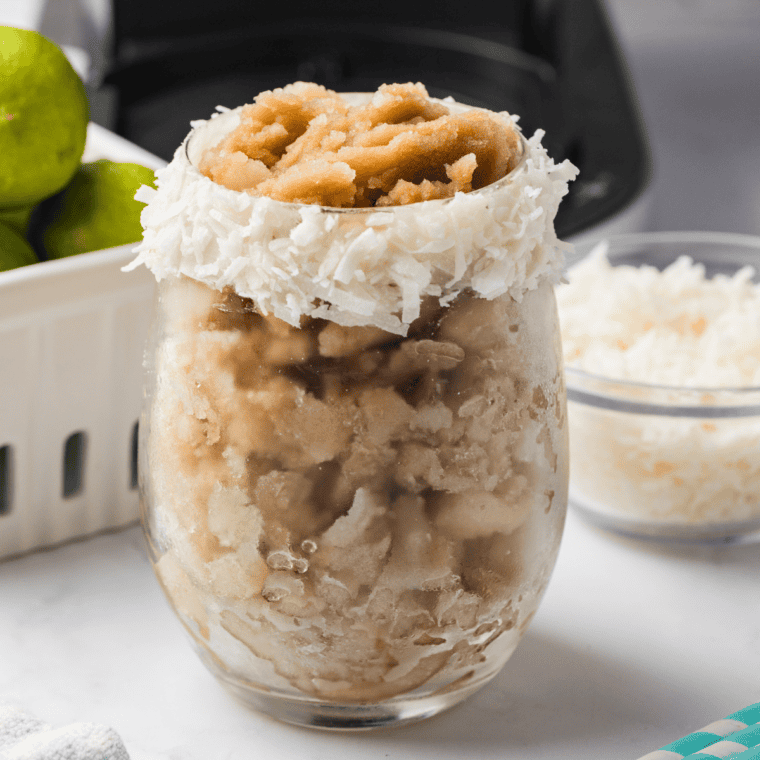 Frosty Ninja Creami Dirty Dr Pepper Slush with coconut and lime served in a clear glass with a straw

