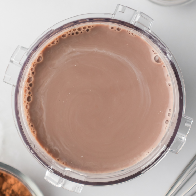 Pouring hot chocolate mix and milk into a Ninja CREAMi pint container up to the drinkable fill line.