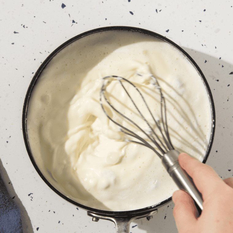 Heavy cream and milk heating in a saucepan with mini marshmallows melting to create a smooth, marshmallow-infused cream.